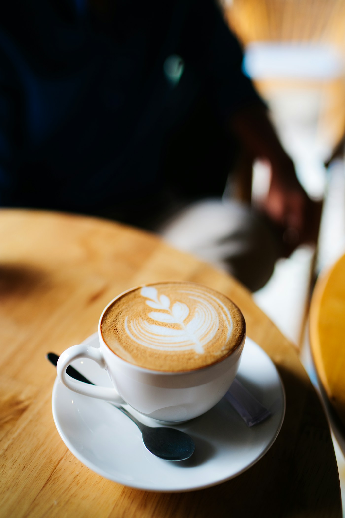 Latte with leaf-pattern latte art in a white cup on a timber table