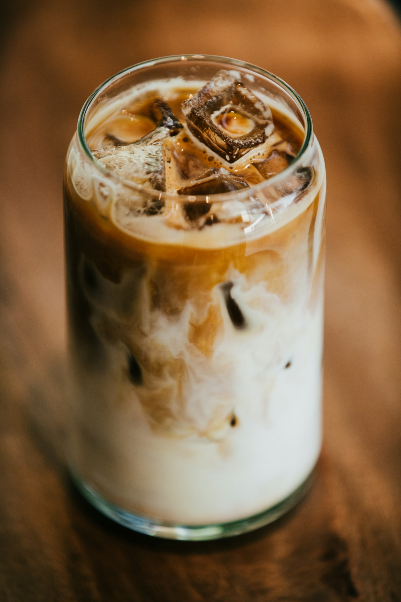 Iced latte in a tall glass with layered milk and coffee on a wooden table